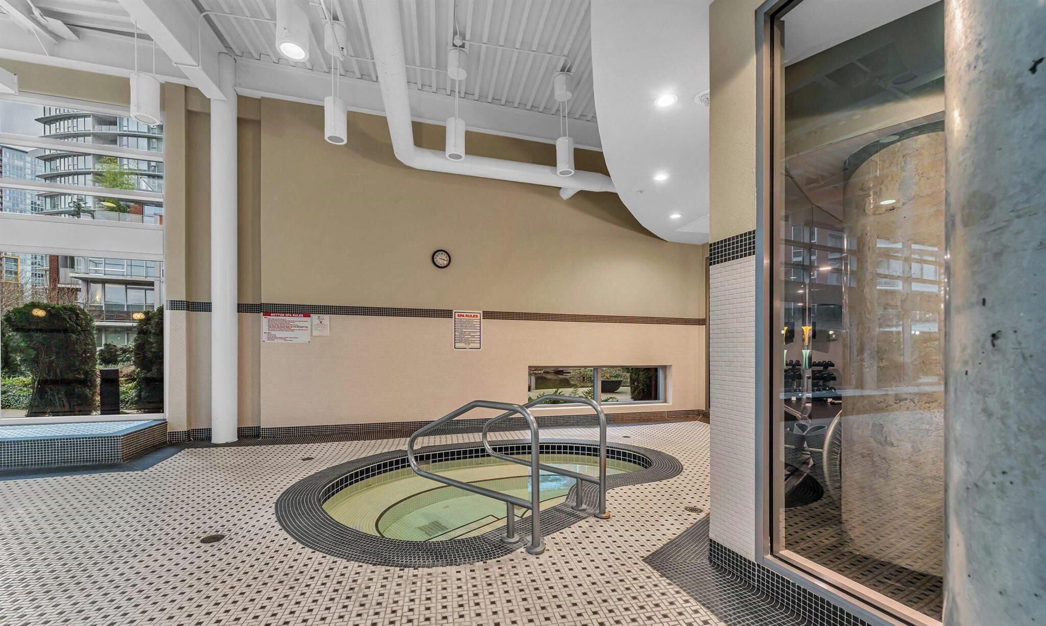Una piscina interior con suelo de baldosas, un reloj en la pared y un cartel con las normas del spa.