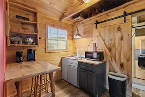 A wooden interior with a kitchen area, including a bar stool, a coffee maker, a microwave, and a sink.