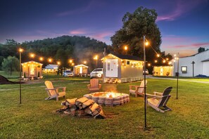 Ein Campingplatz mit Sitzgelegenheiten im Freien, einem Feuerkorb und Lichterketten.