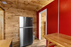 Eine kompakte Küche mit einem Edelstahl-Kühlschrank mit zwei Türen, Holzvertäfelung, einer roten Akzentwand und einem Holztisch.