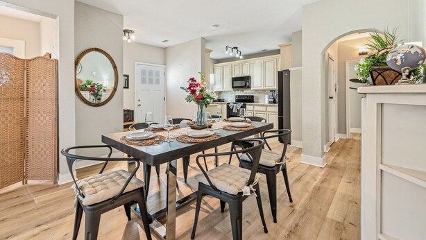 A dining area with a wooden table, four chairs, a vase with flowers, and a kitchen in the background. - Home near NRG - Sleep 8 - WolrdCup ready (Houston)