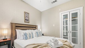 A bedroom with a bed, a nightstand, a lamp, a door with glass panels, and a wall-mounted picture. - Home near NRG - Sleep 8 - WolrdCup ready (Houston)
