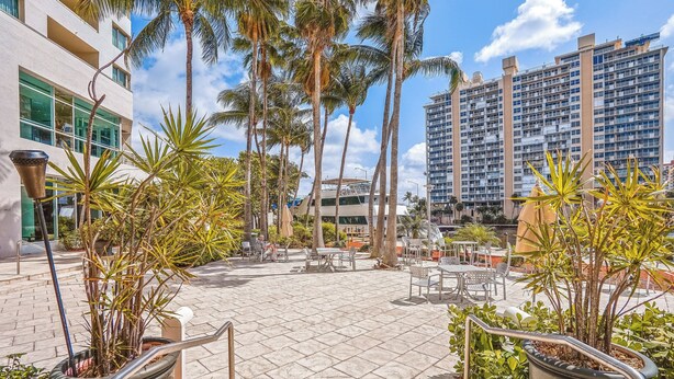 A courtyard with outdoor seating, palm trees, and modern buildings in the background.