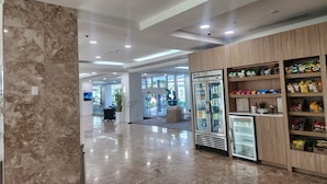A clean, modern lobby with a marble floor, a refrigerated display case, and a wooden shelving unit with snacks.