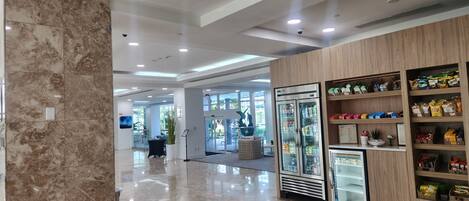 A clean, modern lobby with a marble floor, a refrigerated display case, and a wooden shelving unit with snacks.