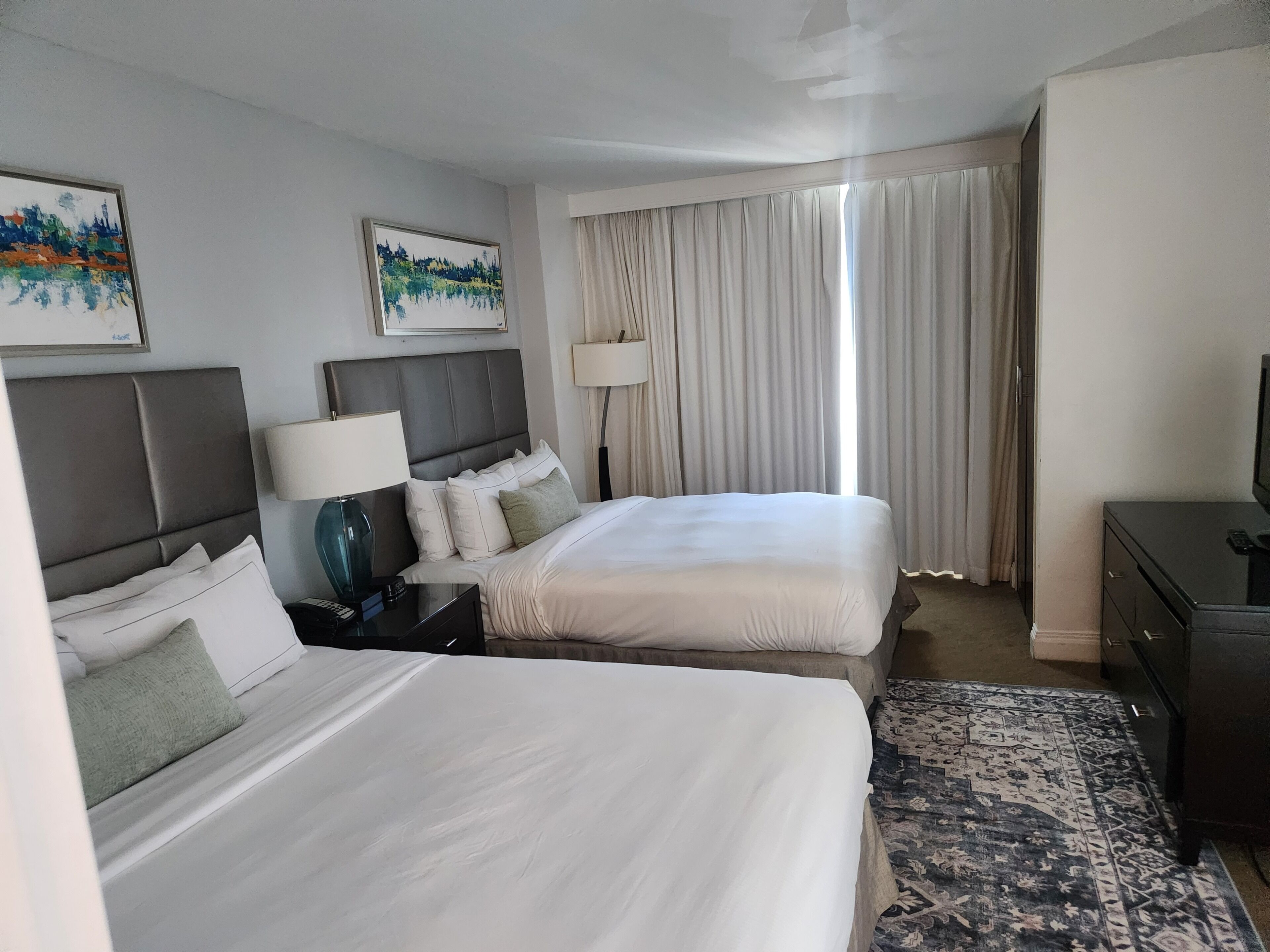 Habitación de hotel con dos camas, un escritorio, televisor y ventana con cortinas.