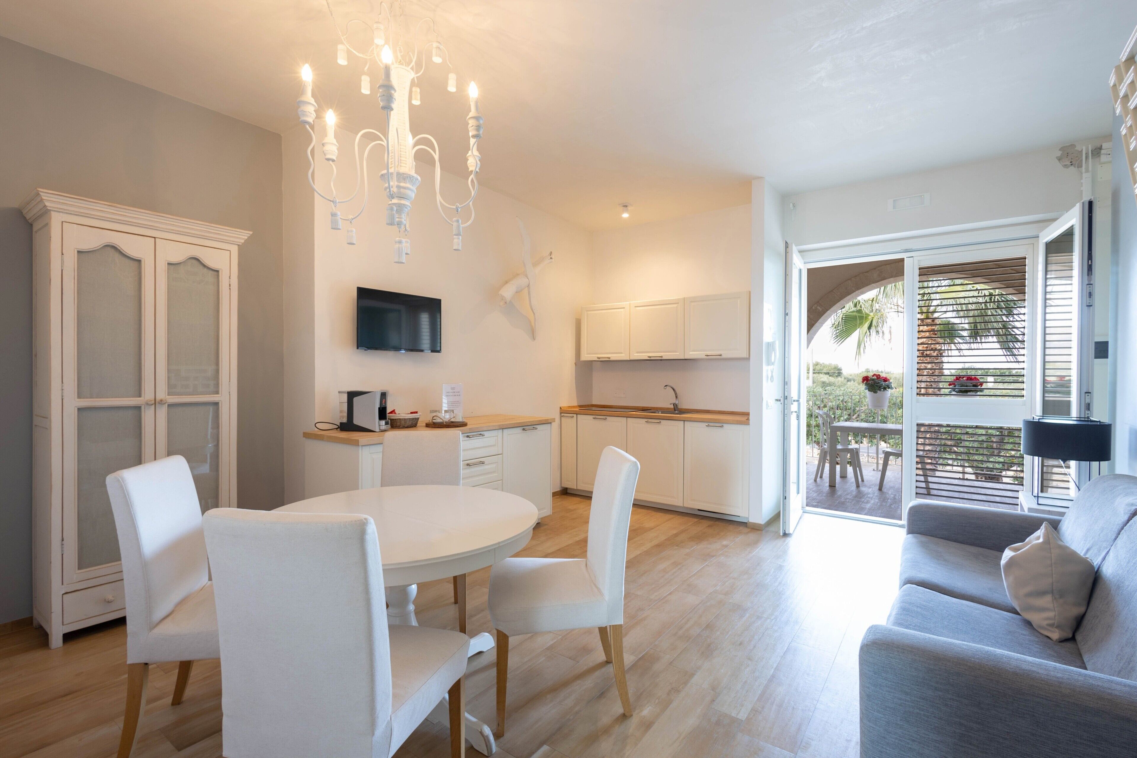 A modern kitchen with white cabinetry, a dining area with a round table and chairs, and a balcony with outdoor seating.