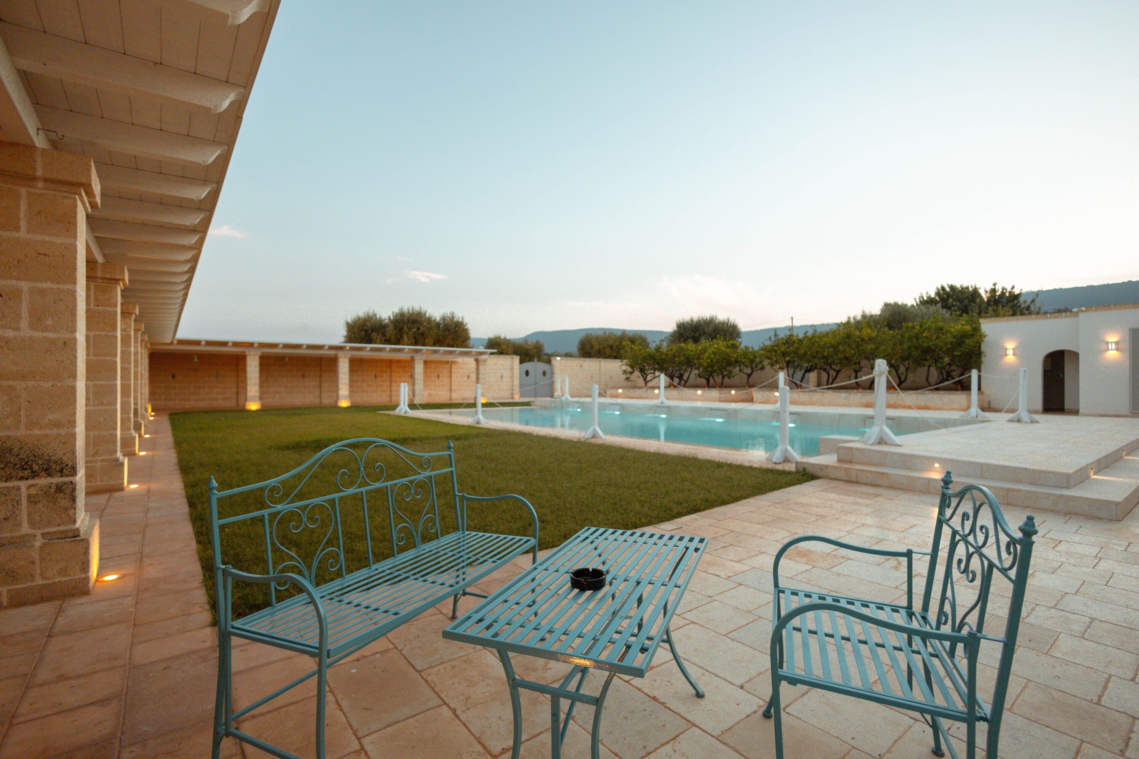 Un patio con due panchine in metallo, un tavolino e una piscina sullo sfondo.