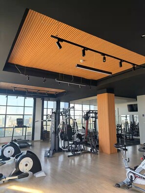Une salle de sport équipée de matériel d’exercice, dotée de grandes fenêtres et d’un plafond en bois au design original.