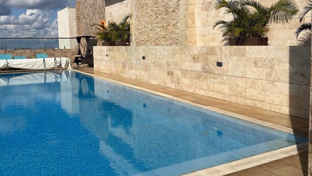 Una piscina con vista despejada al mar, un muro de piedra y algunas plantas en macetas.