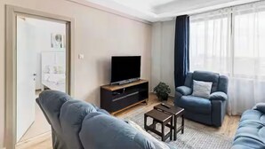 Una sala de estar moderna con un televisor de pantalla plana, un sofá, una silla y una pequeña mesa de centro.