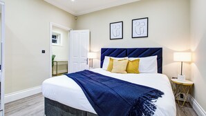 A neatly made bed with a blue throw, two bedside lamps, and framed artwork on the wall. - Hybrid Resi Battersea (London)