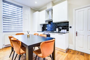 Eine moderne Küche mit weißen Schränken, einer schwarzen Arbeitsplatte und einem Holzespeisetisch mit orangefarbenen Stühlen.