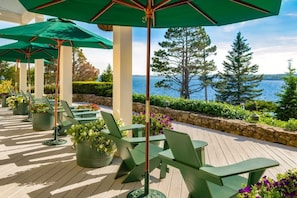 Een terras met groene stoelen en parasols, met uitzicht op een waterpartij.