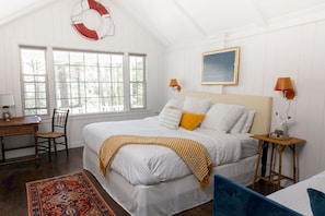 A bedroom with a large bed, a desk, a chair, a window, and a life preserver on the wall.