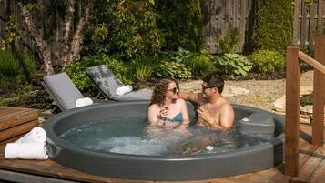Un bain à remous où peuvent se détendre deux personnes, entouré d’une terrasse en bois et de verdure.