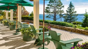 Une terrasse avec des chaises et des parasols verts, donnant sur une étendue d’eau et des arbres.