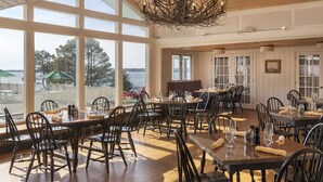 Un espace repas comprenant plusieurs tables et chaises, de grandes fenêtres donnant sur l’extérieur et un lustre.