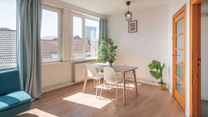 Een kamer met een eettafel, stoelen, een potplant, een bank en een schuifpui.
