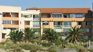 A multi-story hotel with balconies, palm trees, and a sandy foreground. - Spacious Coastal Stay for 8 in Cap D'agde (Agde)