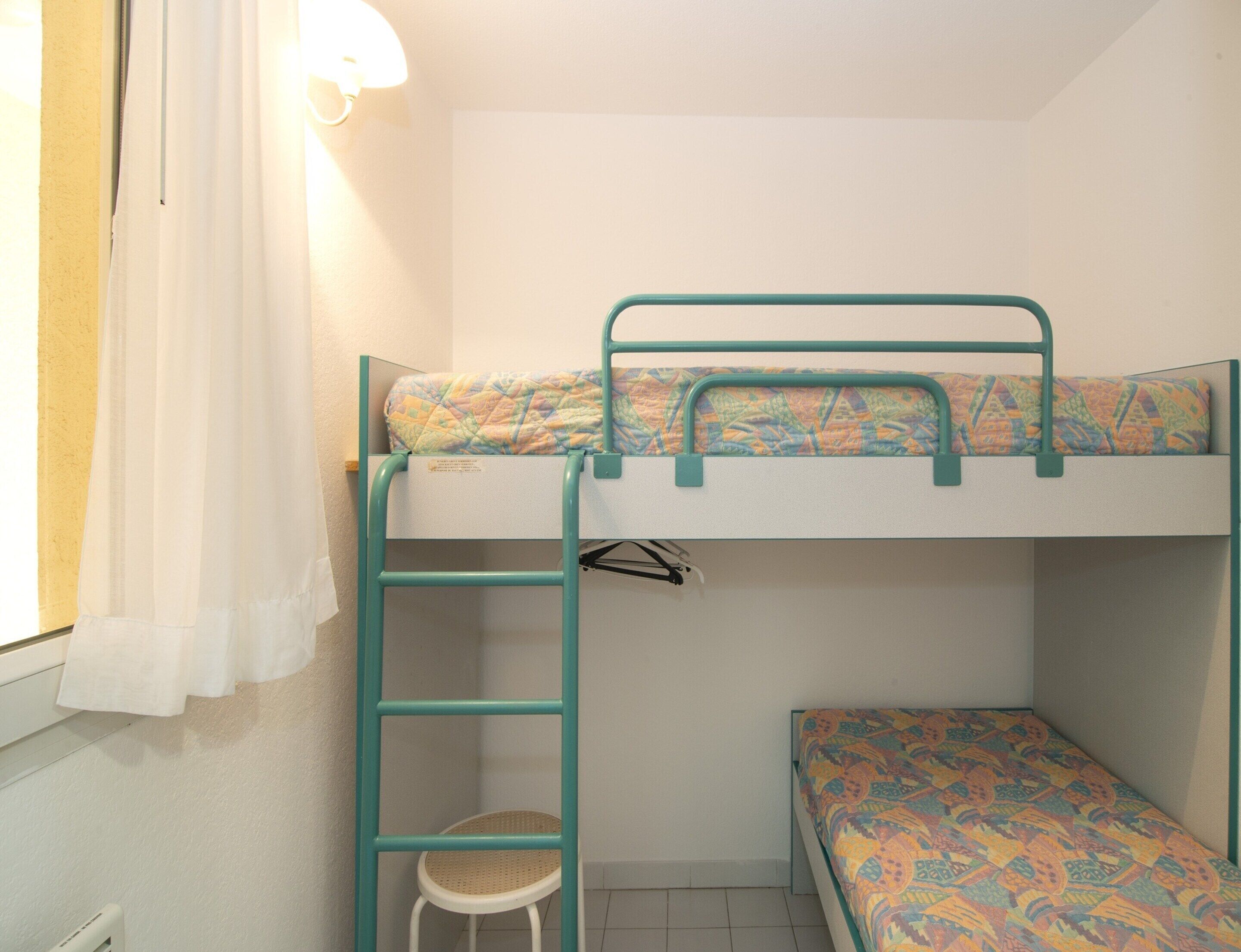 A bunk bed room with a ladder, a small stool, and a window with curtains.