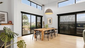 A spacious dining area with a wooden table and chairs, large windows, and a view of the outdoors. - Surfers Rest in Surf Beach (Surf Beach)