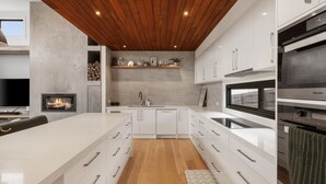 A modern kitchen with white cabinetry, a wooden ceiling, a built-in fireplace, and a large island with drawers. - Surfers Rest in Surf Beach (Surf Beach)