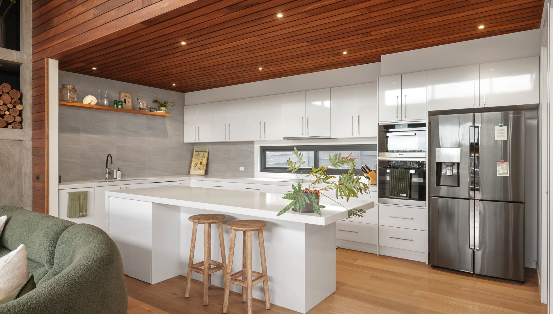 Una cocina moderna con armarios blancos, un refrigerador de acero inoxidable, taburetes de madera y una isla grande.
