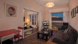 A hotel room with a sofa, a dining table, a TV, and a balcony with a view. - Acropolis View for Groups - 100% Athens experience (Athina)