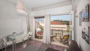 A room with a dining table, chairs, a sofa, a small table, and a view through a glass door. - Acropolis View for Groups - 100% Athens experience (Athina)