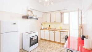 A kitchen with white cabinets, a stove, a refrigerator, and a red table. - Acropolis View for Groups - 100% Athens experience (Athina)
