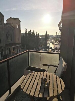 Een balkon met een tafel en stoelen, met uitzicht op een straat met gebouwen en bomen.