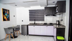 A compact kitchen with a dining area, a refrigerator, and a trash bin.