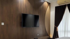 A modern hotel room with a large bed, a flat-screen TV mounted on a wooden wall, and a built-in bedside table.