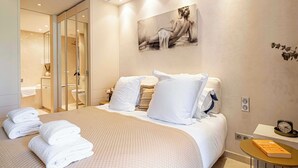 A hotel room with a bed, towels, a painting, a clock, and a bedside table. - Modern Appartement a/c 2br/4p - Cannes (Cannes)