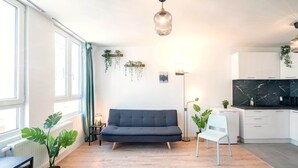 Ein modernes Wohnzimmer mit einer Couch, einem Esstisch, einem Sessel, einer Stehlampe und einer Küchenzeile mit Schränken und einer Arbeitsplatte.