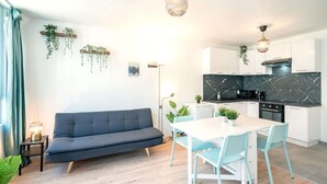 Eine moderne Küche mit weißen Schränken, einer Marmor-Spritzschutzwand und einem Essbereich mit weißem Tisch und blauen Stühlen.