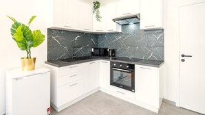 Eine moderne Küche mit weißen Schränken, einer schwarzen Marmor-Spritzschutzleiste, einem Einbauofen und einem Blumentopf.