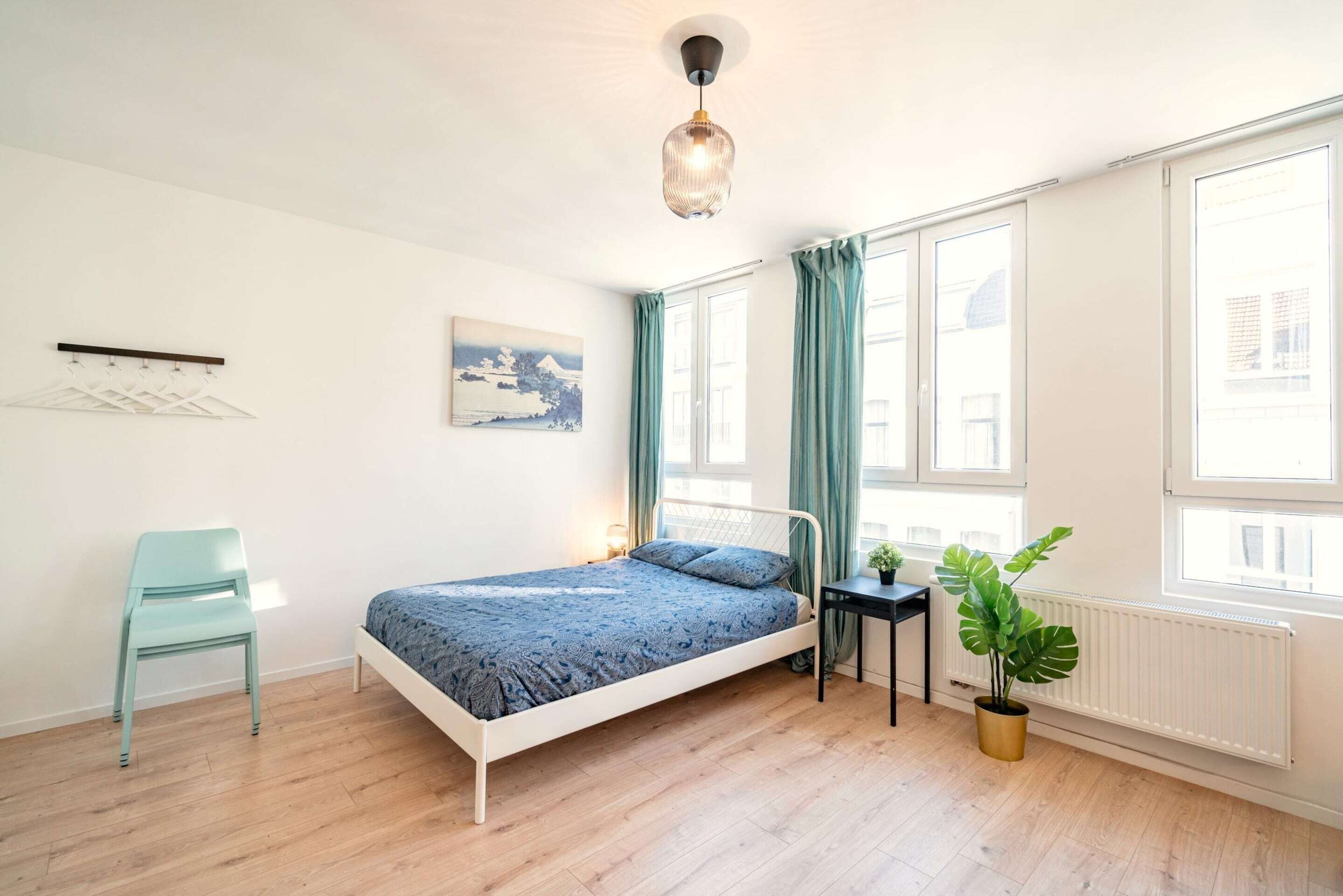 Une chambre avec un lit, une chaise, une table, une plante en pot et une fenêtre.