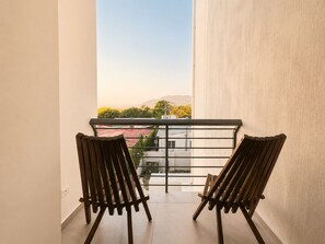 Ein Balkon mit zwei Holzstühlen, einem Metallgeländer und Blick auf Gebäude und Berge in der Ferne.