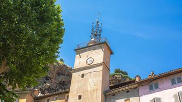 Una torre con un orologio e una croce in cima, circondata da edifici con persiane.
