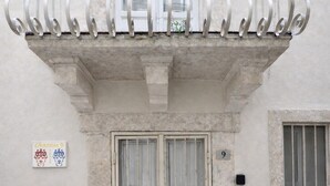 Un edificio con un balcón, un acceso doble con celosía metálica y un ventanal pequeño a la derecha.