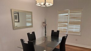 A dining room with a glass table, black chairs, a mirror, and a window with blinds. - Luxurious House - 4 Bedrooms, 1 King, 3 Queen, 1 Singe bed Near Airport sq1 (Mississauga)
