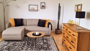 A living room with a sofa, a coffee table, a cactus, a wooden dresser, and a floor lamp. - Modern vacation apartment in Dülmen: close to the city with a balcony view of the countryside (Dülmen)