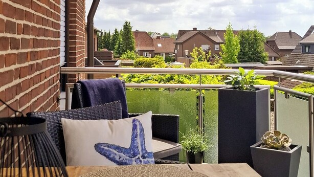 A wooden deck with a round woven mat, a metal birdcage, and a blue pillow. - Modern vacation apartment in Dülmen: close to the city with a balcony view of the countryside (Dülmen)
