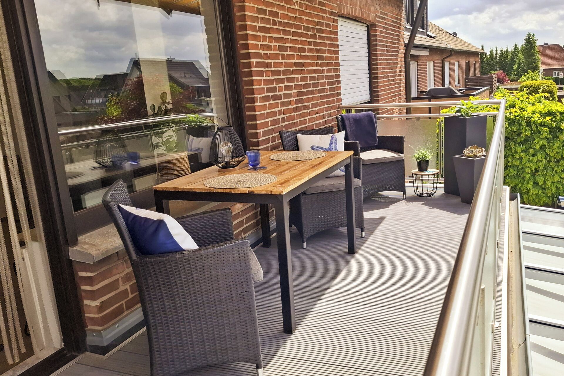 Een balkon met een houten tafel en rieten stoelen, een glazen deur en een bakstenen muur.