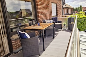 A balcony with a wooden table and wicker chairs, a glass door, and a brick wall.