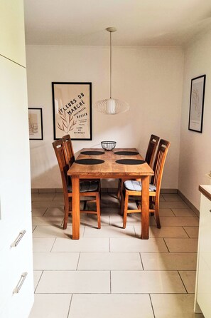 A dining area with a wooden table, four chairs, a hanging light fixture, and framed artwork on the walls.