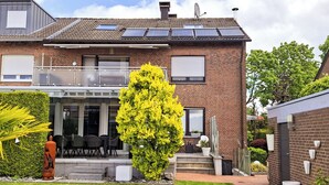 A two-story house with a patio, a large yellow flowering tree, and a brick exterior. - Modern vacation apartment in Dülmen: close to the city with a balcony view of the countryside (Dülmen)
