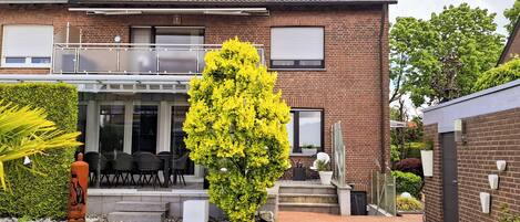 Una casa de dos pisos con un patio, un gran árbol amarillo con flores y fachada de ladrillo.